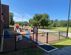 A fenced-in playground with a play structure and a grassy area.