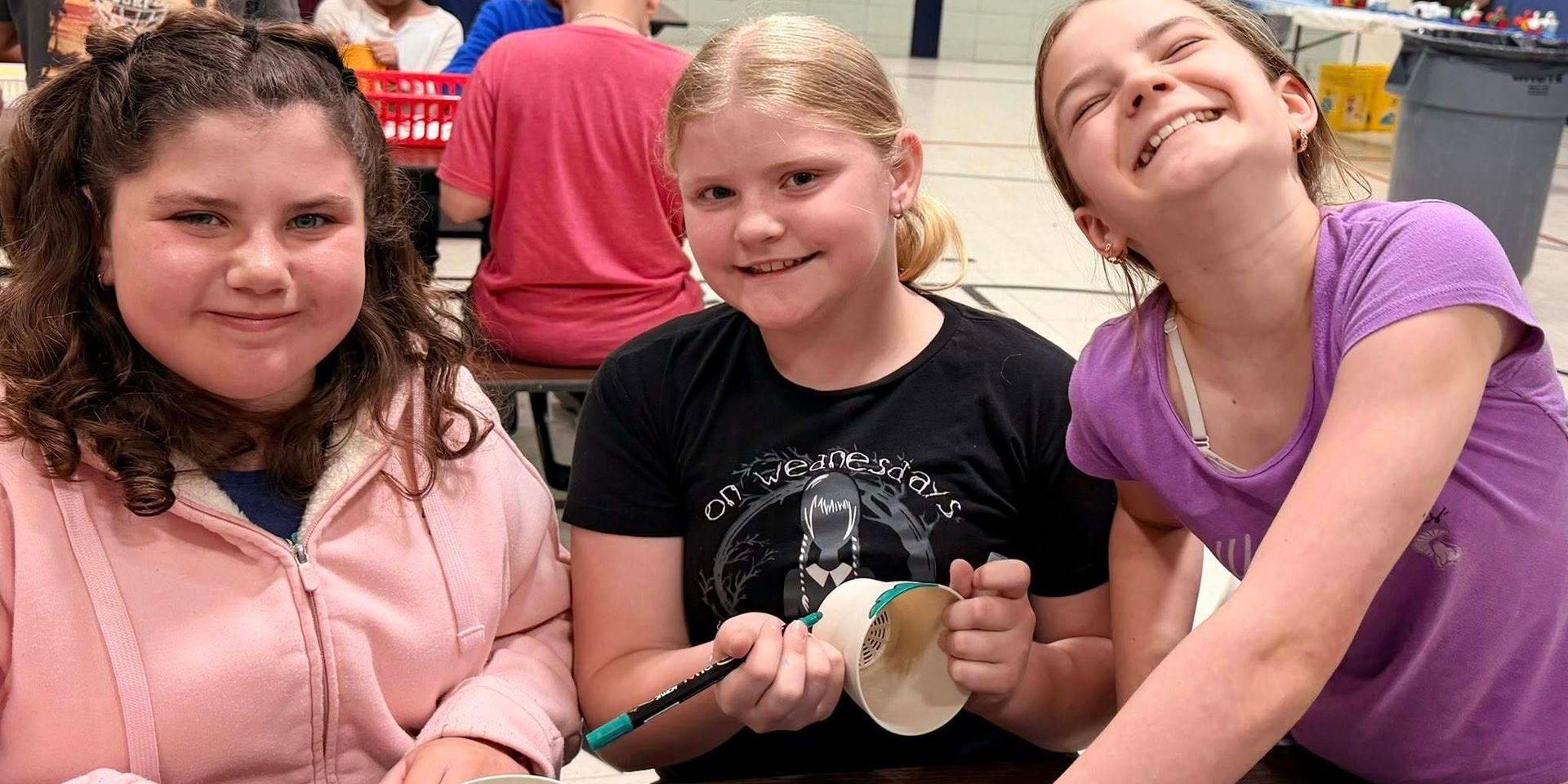 Three girls posing happily while crafting at a table.