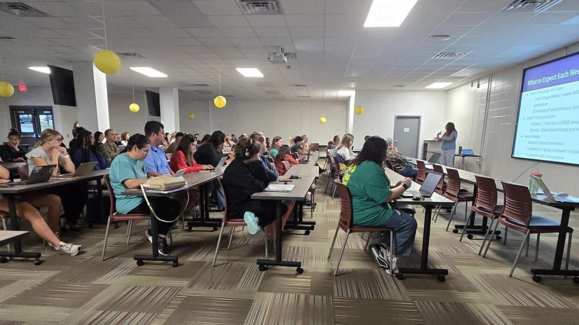 Large audience observing a presentation in a classroom filled with yellow decor.
