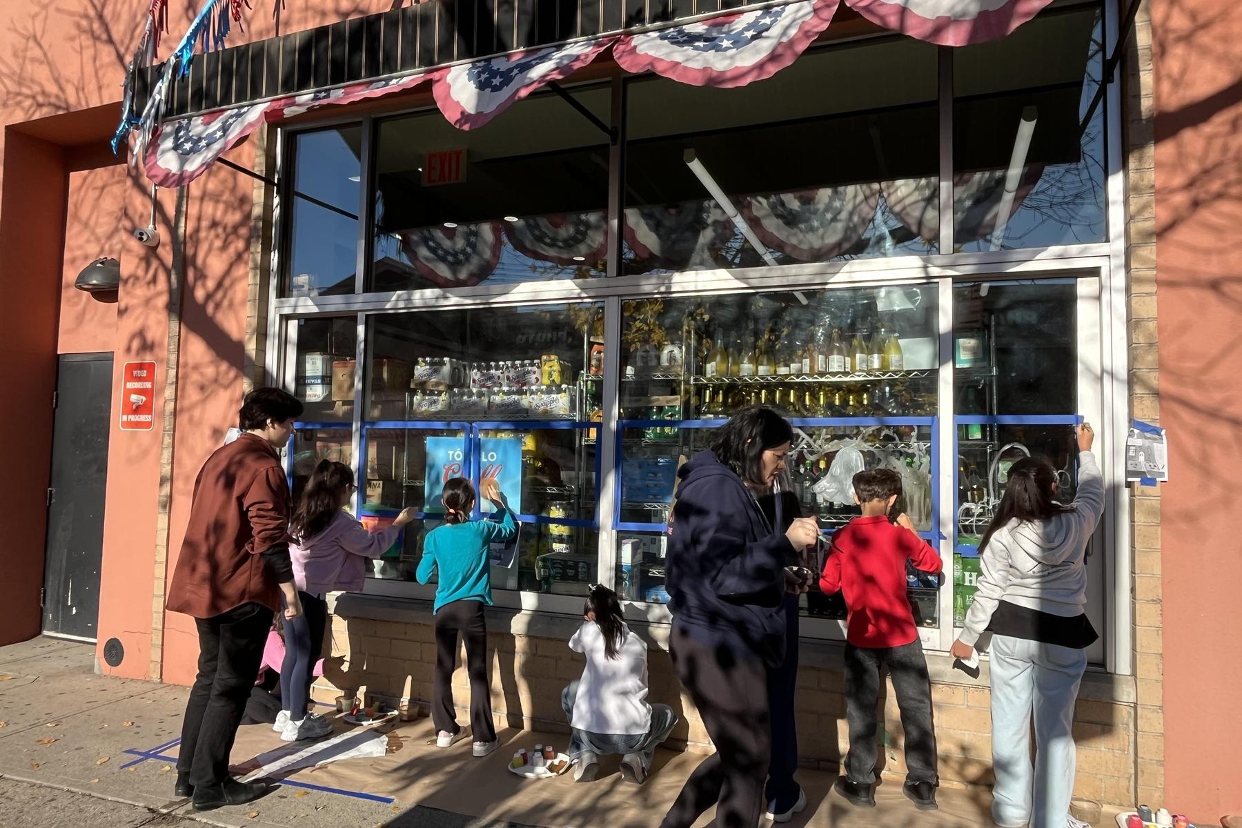 People engaged in painting a storefront window, with decorative elements above.