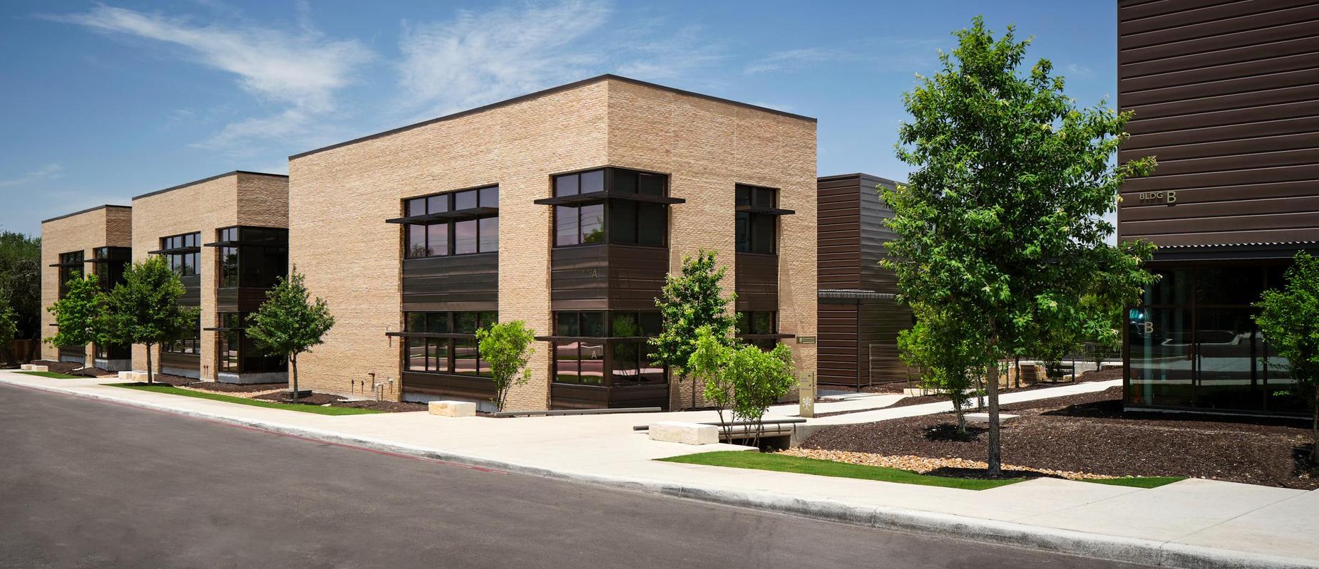 Modern brick buildings with large windows and trees lining the walkway.