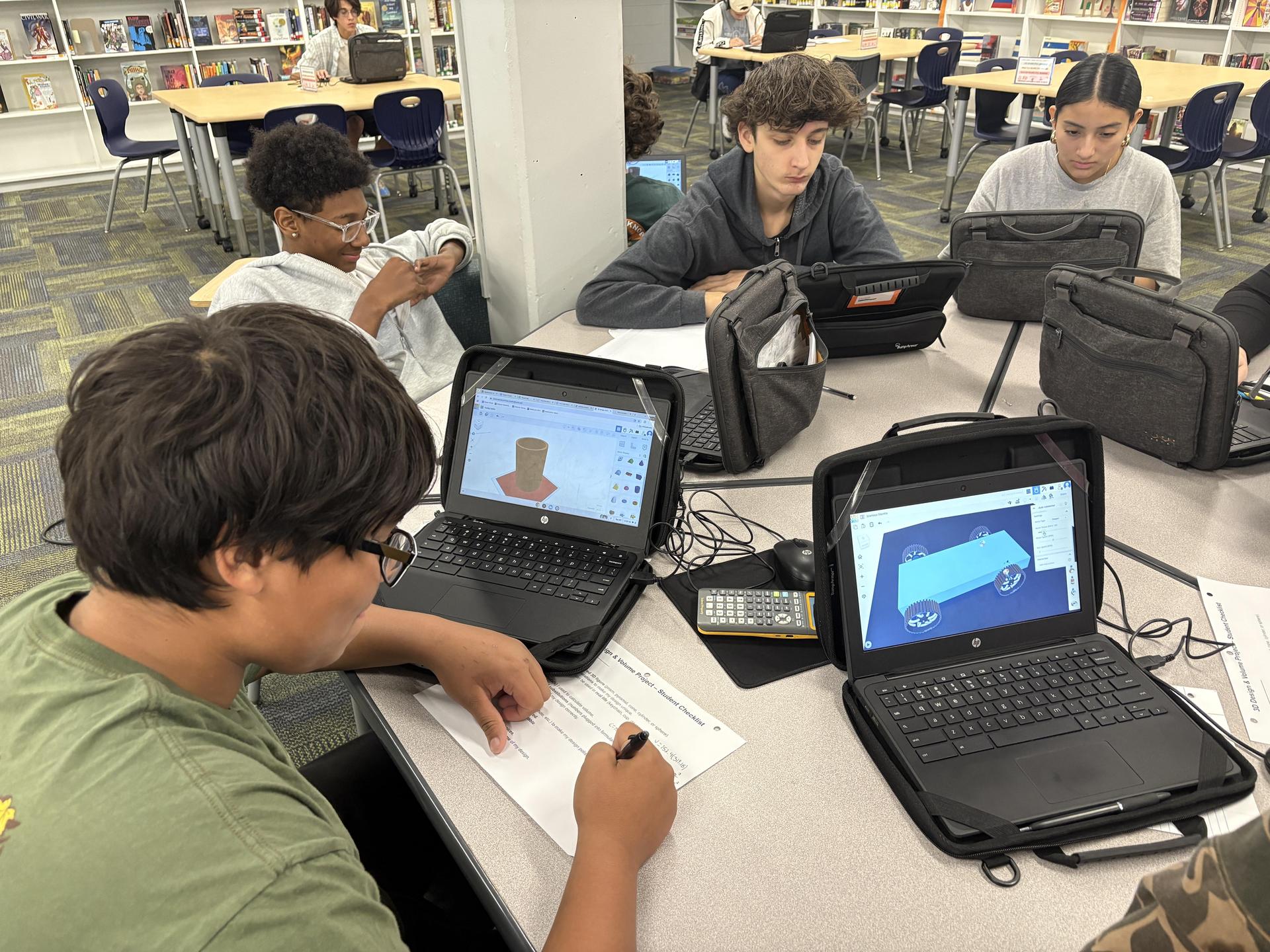 Four students working on laptops and notepads, collaborating in a library.