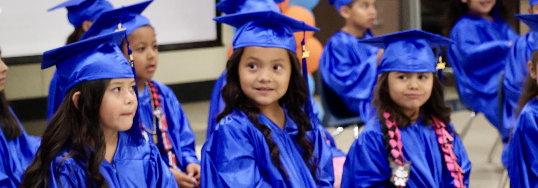 Kindergarten Promotion. 3 students sitting in caps and gowns.