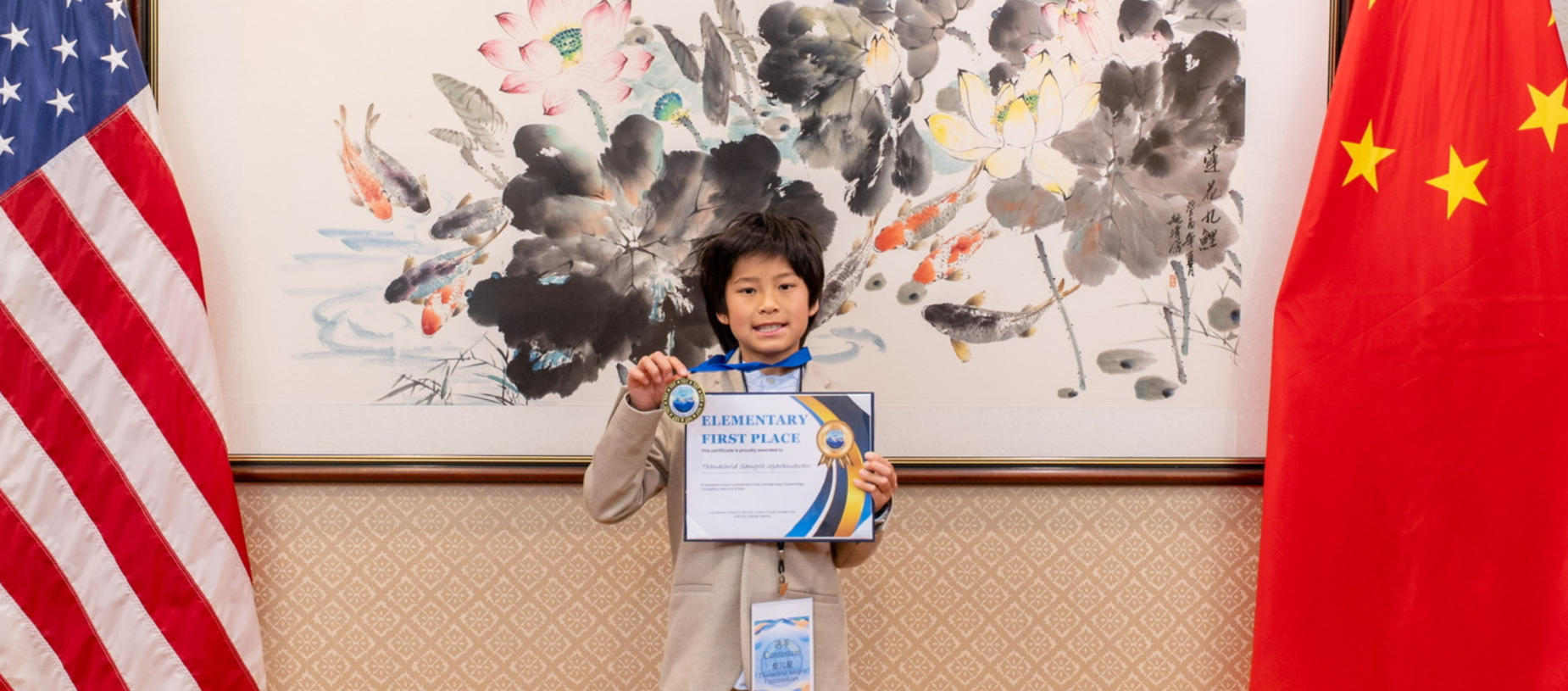 A young boy holding a first place certificate in front of Chinese and American flags.