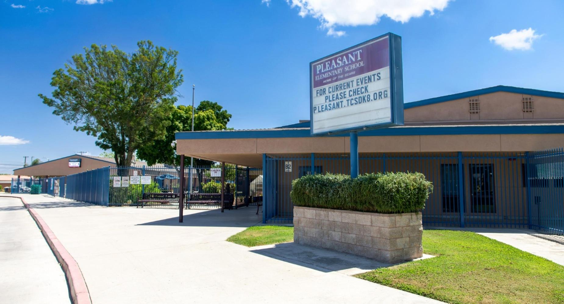Pleasant School building with sign, trees, and open walkway under a clear blue sky.