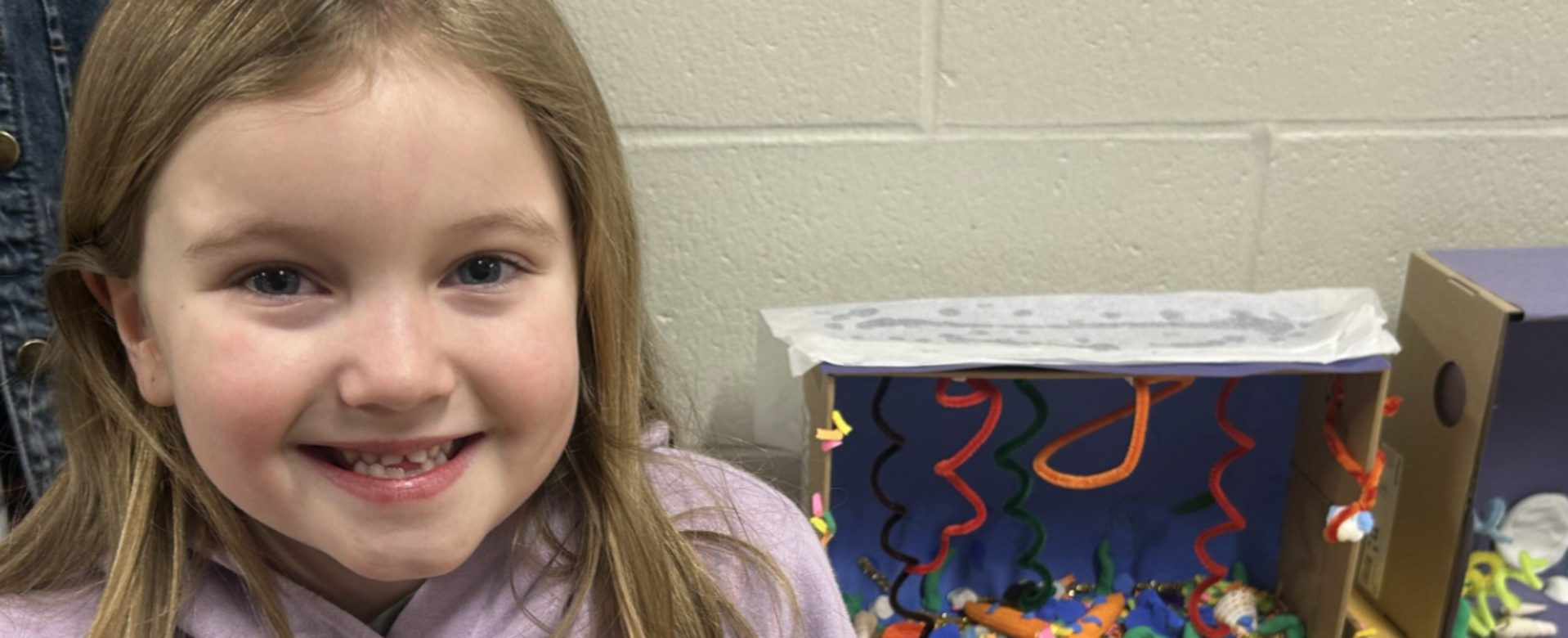 Girl smiling beside a colorful craft project with decorations and a paper star.