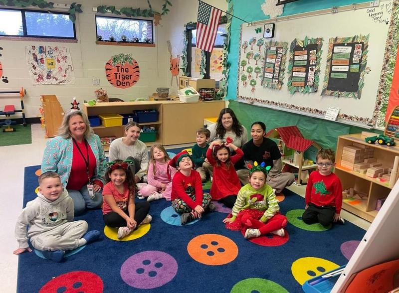 Teacher and students sitting on a colorful rug in a classroom
