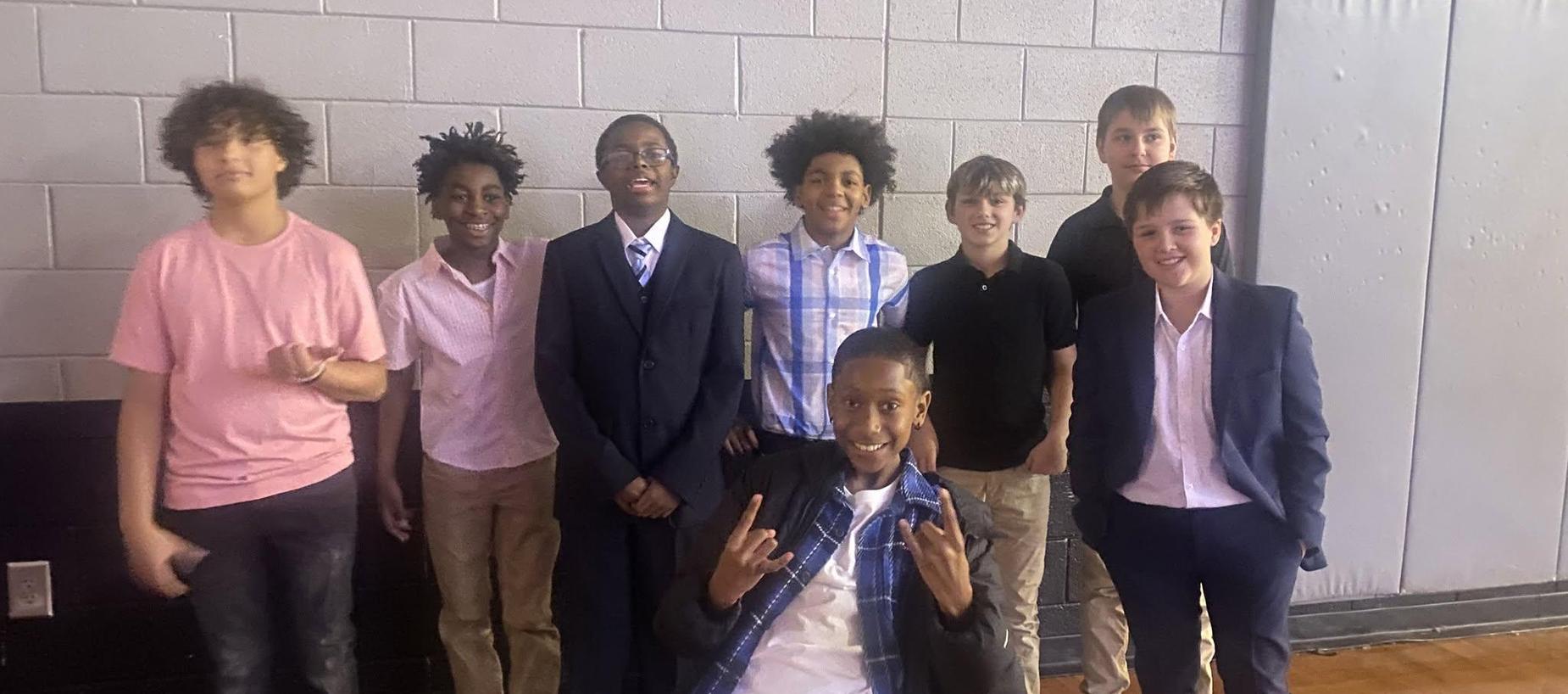 A group of young boys smiling together in formal attire indoors.