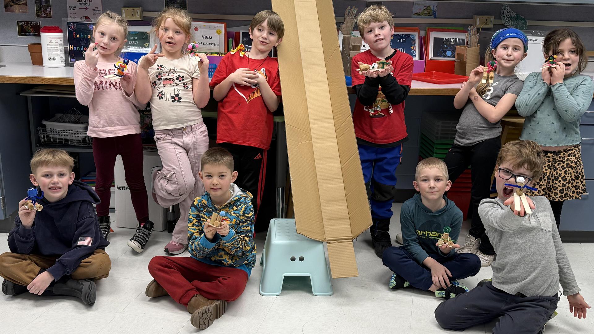 Group of children holding crafts in a classroom setting.