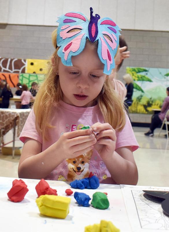 A girl wearing a butterfly headband molds colorful clay at a table.
