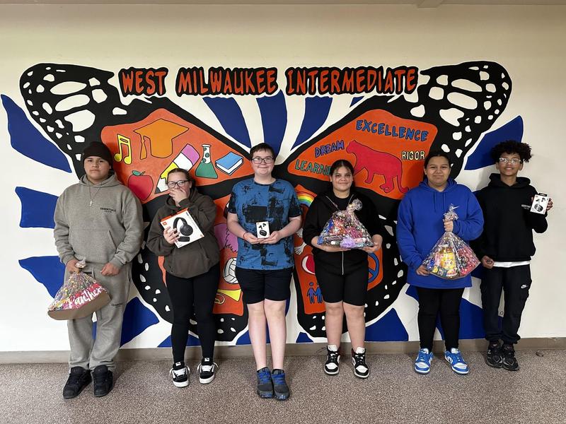 Students holding prizes in front of a colorful school mural.