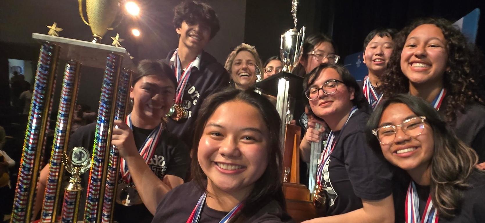 Group of students celebrating with trophies and medals at an awards ceremony.