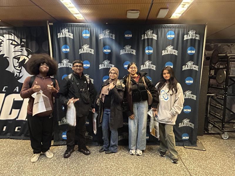 A group of five people posing in front of a school banner.