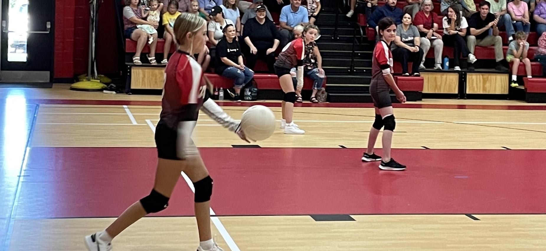 A volleyball player serves the ball while two players look on.