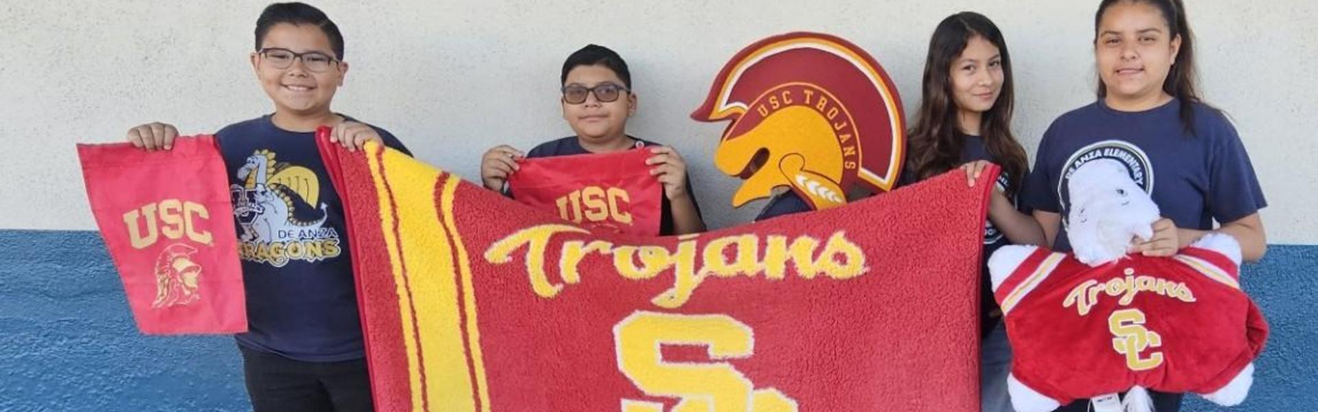 Four individuals holding USC Trojans merchandise, including a towel and a blanket.