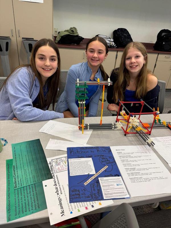 Three female students smile surrounding their K'Nex prototype at the STEM Design Challenge.