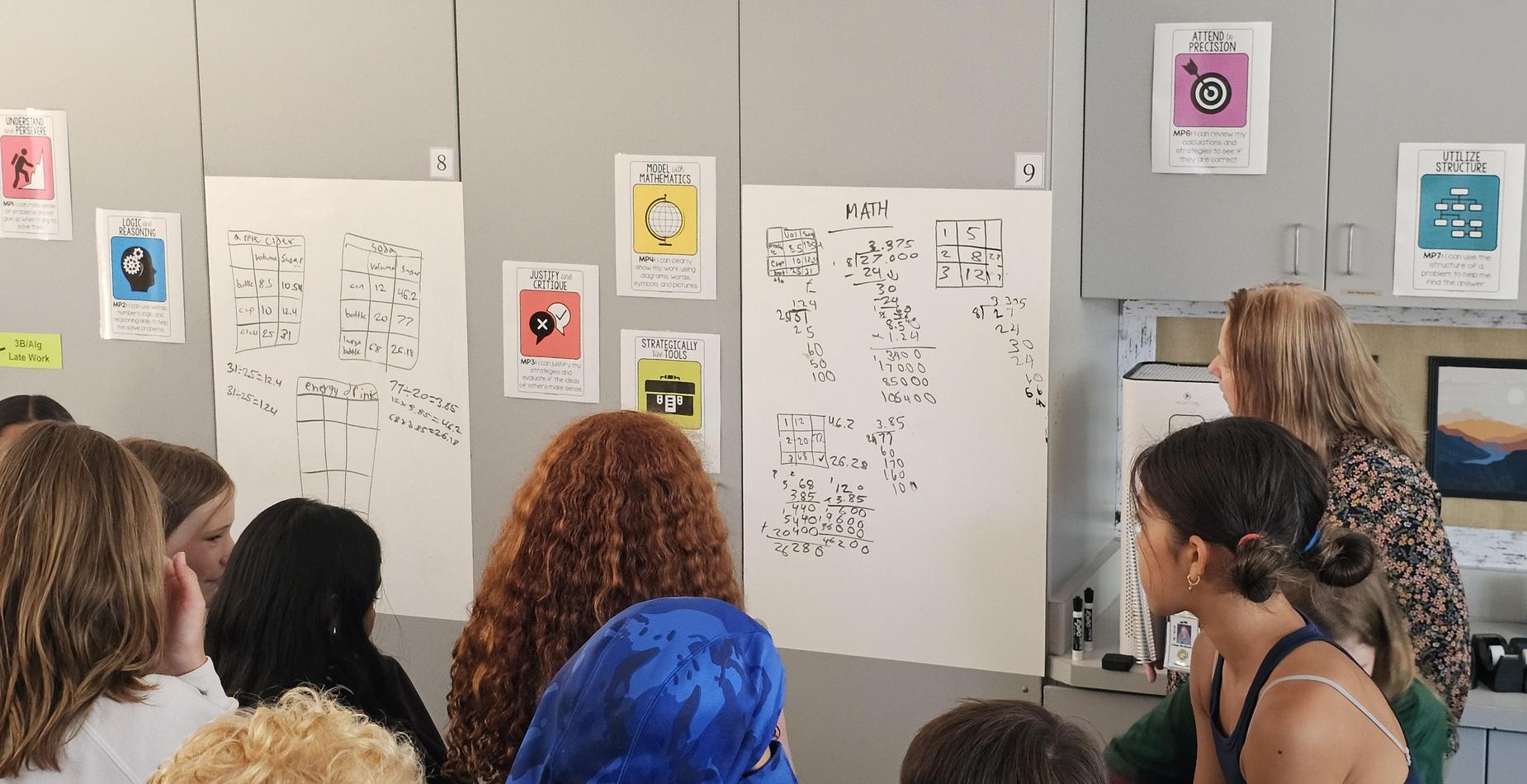 Students gathered at whiteboard around a math problem.