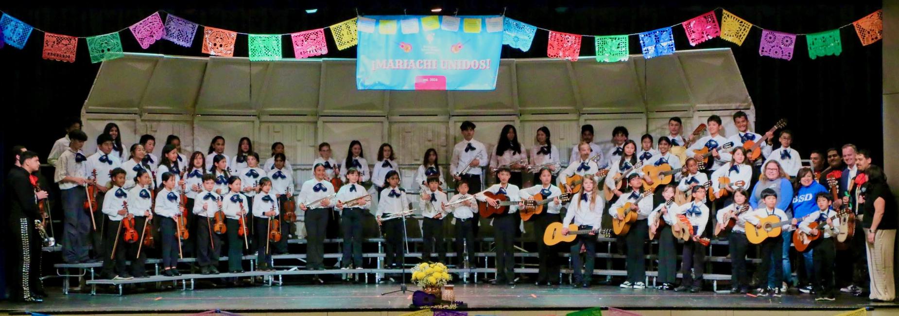 A large group of Mariachi students performing with instruments on stage.