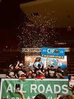 A group of jubilant athletes celebrate a 2025 CIF championship win indoors, wearing matching shirts and hats while lifting a trophy amid a shower of confetti. The backdrop displays the CIF logo and the words "CHAMPIONS" as excited fans capture the moment from the stands.