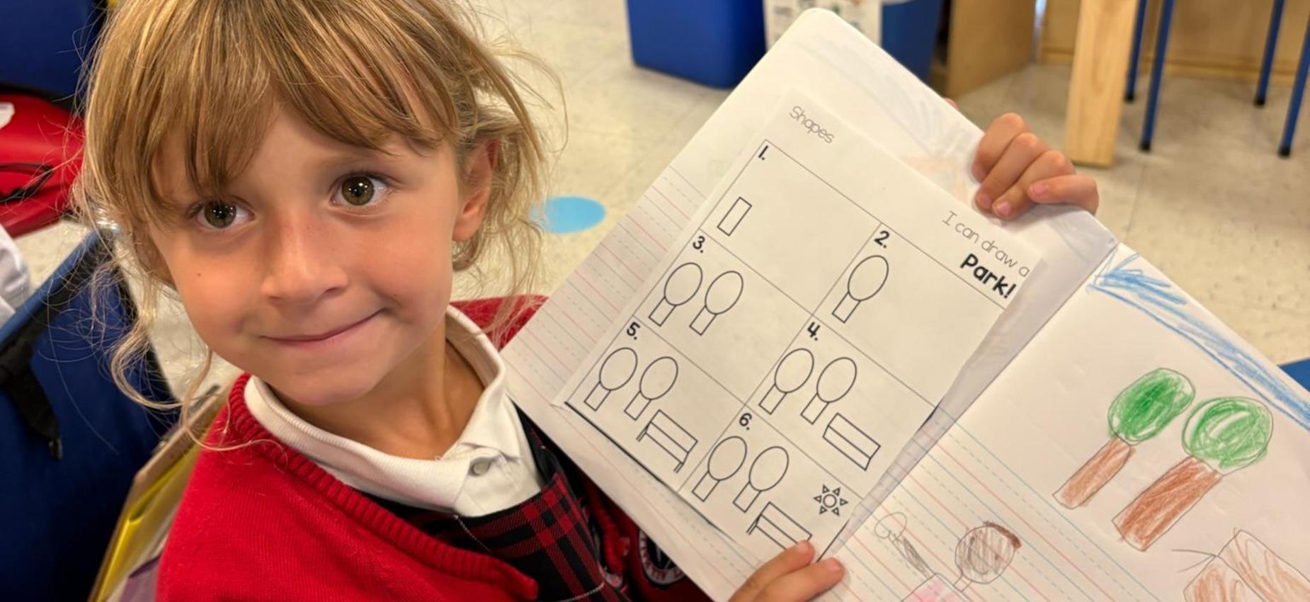 Kindergarten student holds up directed drawing notebook