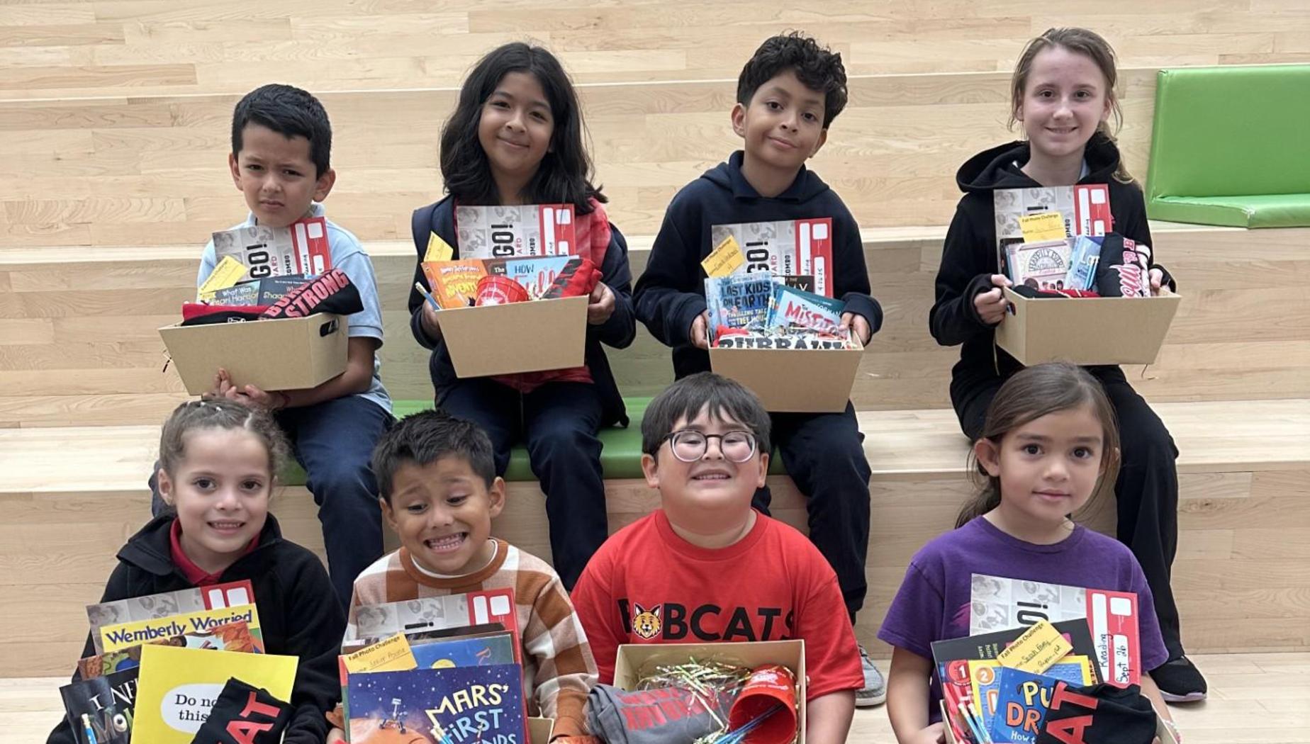 Children sitting on steps, each holding a box of books and school supplies.