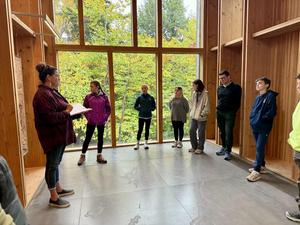 A group listening to a woman presenting in a room with large windows.