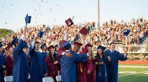 Graduates celebrating at a ceremony, throwing caps in the air with a cheering crowd.