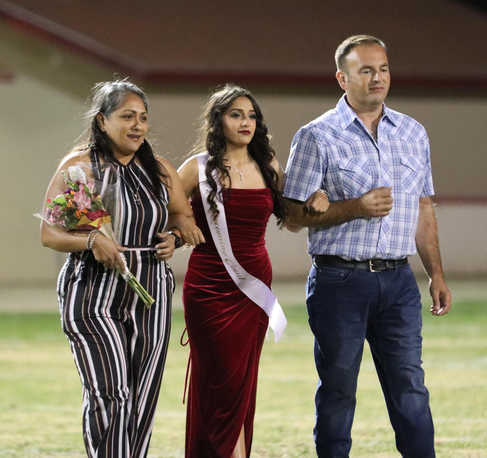 homecoming king and queen candidates walking across the field with their escorts