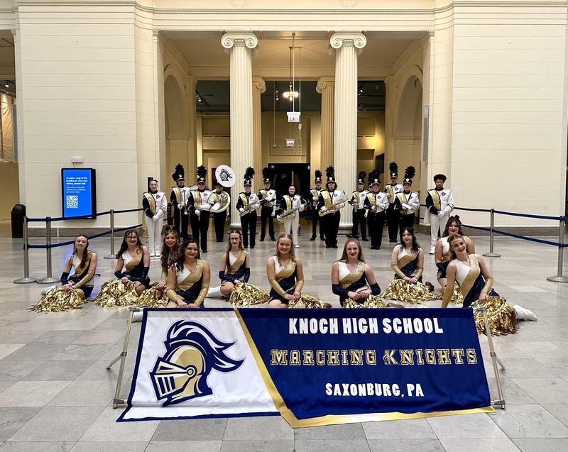 Marching band in uniform with Knoch Marching Band sign in front of them