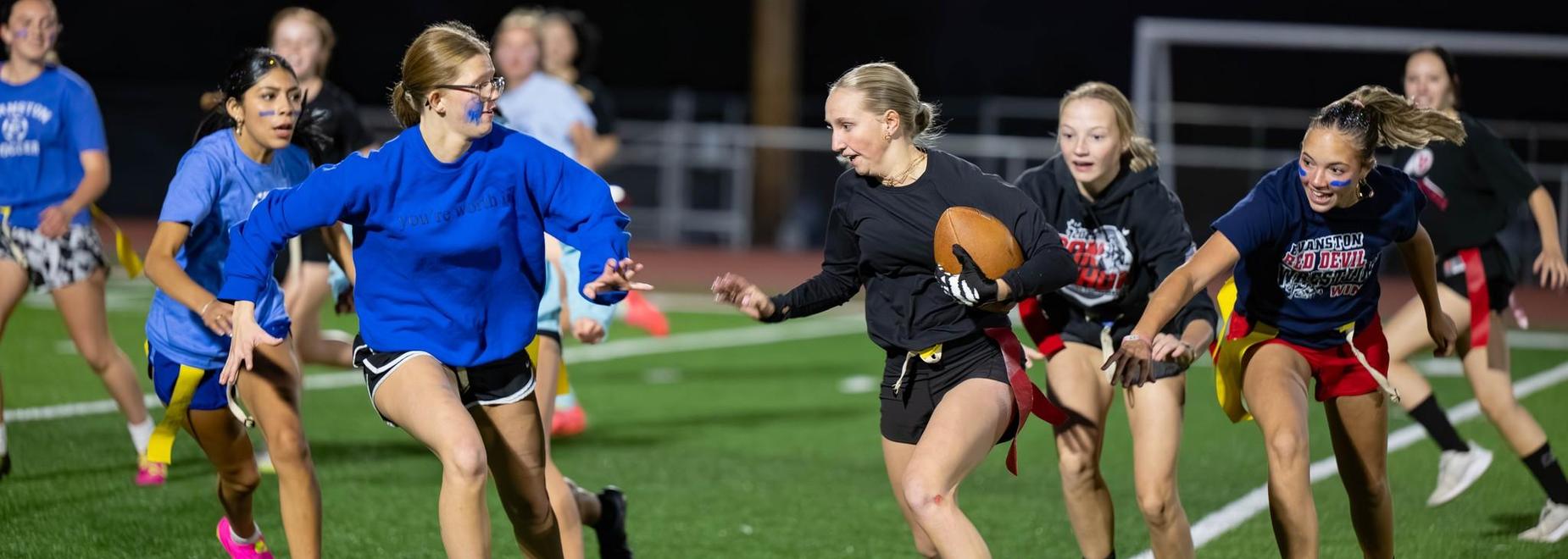 Female athletes playing flag football on a field, showing intensity and teamwork.