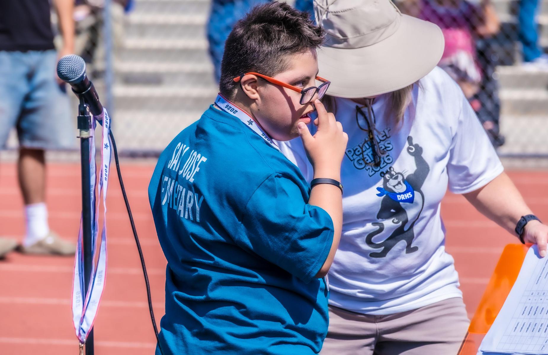 Young student puts finger on his eyeglasses while talking to teacher