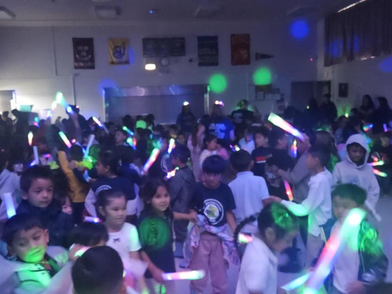 A crowded room of children dancing with glowing light sticks.