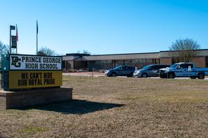 The front of Prince George High School's campus is shown, with vehicles parked at the building near its marquee.