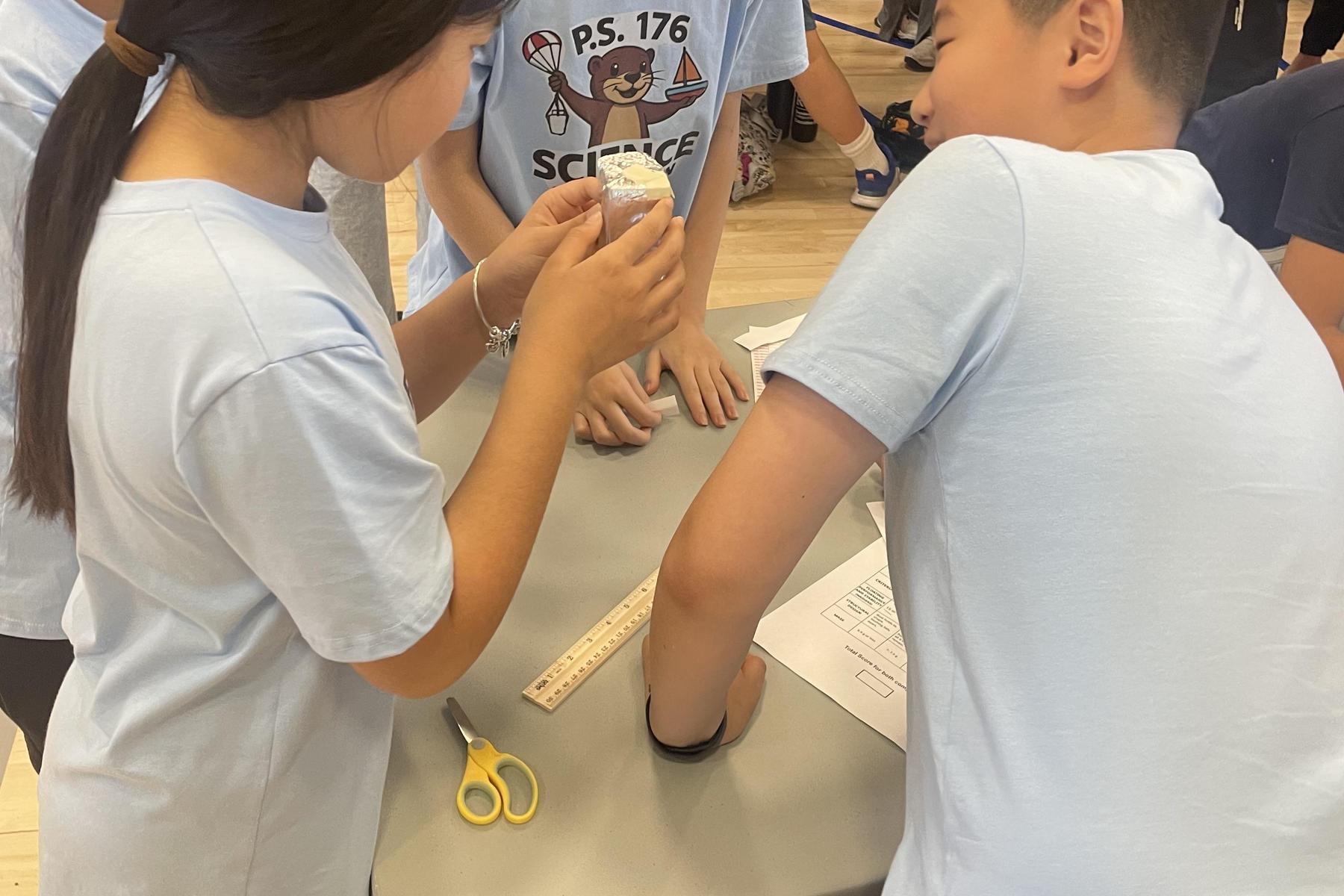 A child holds a cup while others observe, all wearing matching light blue shirts.