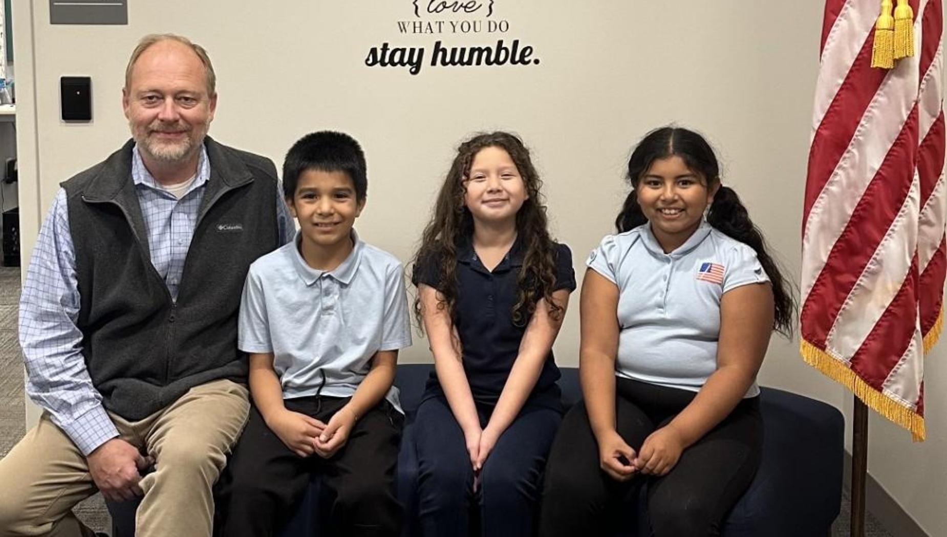 A teacher poses with three students in front of an inspirational wall mural and an American flag.
