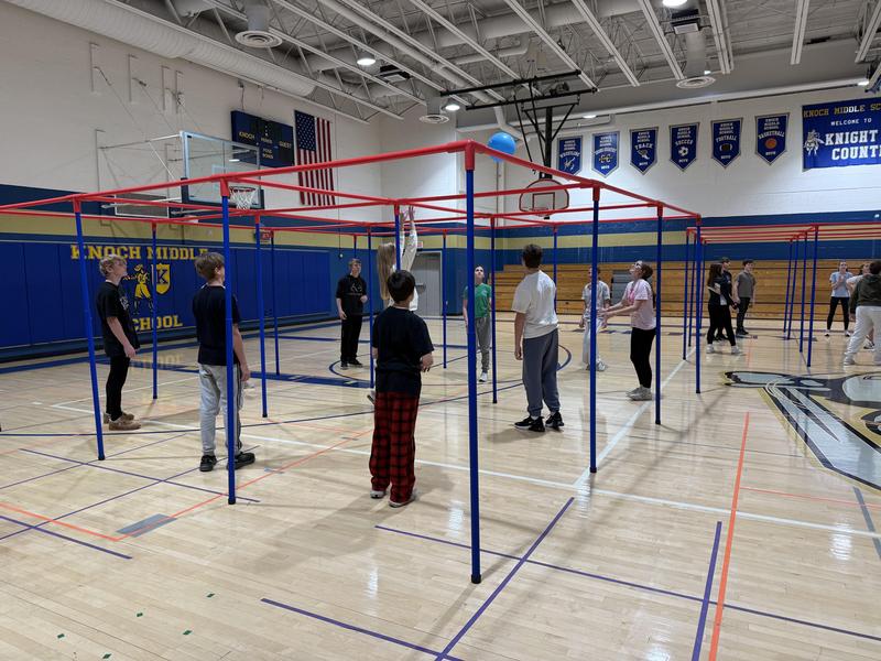 Students standing on a gym floor under a 9 square gym equipment