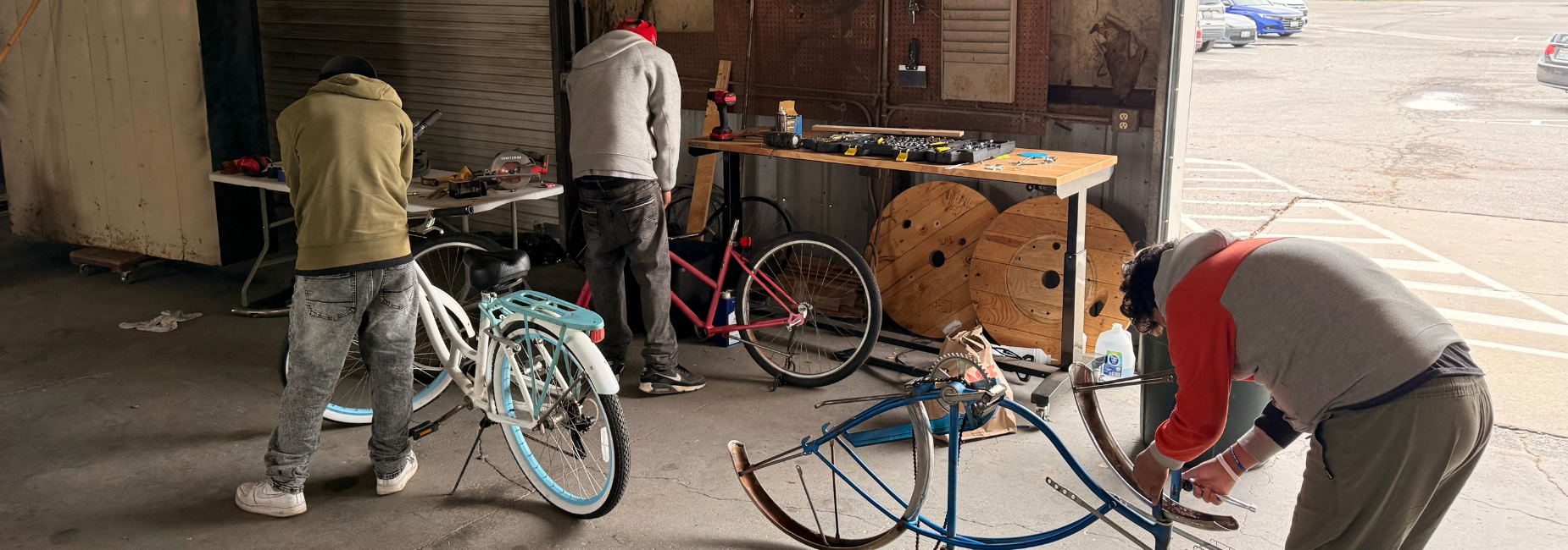 Three individuals work on repairing bicycles in a spacious garage area.