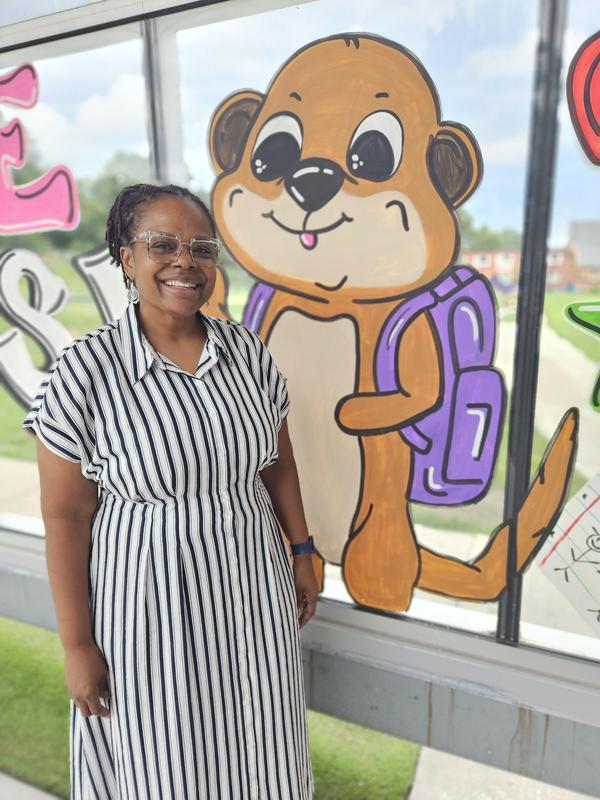 Mrs. Core standing by a Meerkat painted on a window