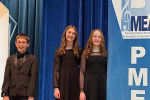 Participants in the PMEA Junior High District Chorus stand on the stage next to the banner