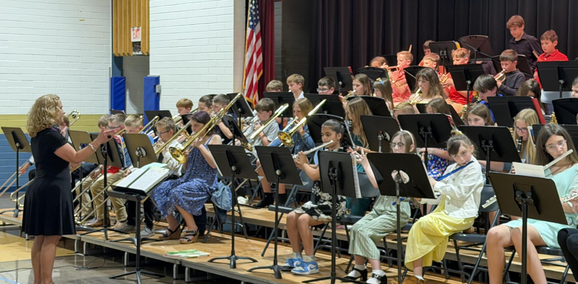 A music director conducting a large band of students playing instruments on stage.