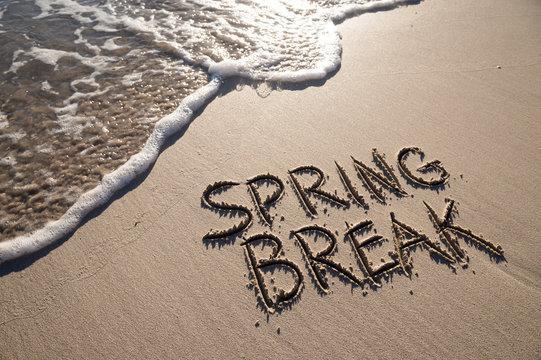 Text saying 'SPRING BREAK' written in sand near the shoreline.