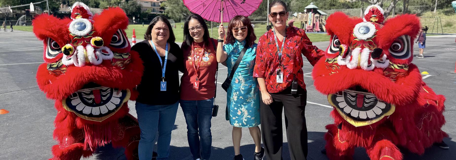 Five women posing with lion dance costumes and a parasol.