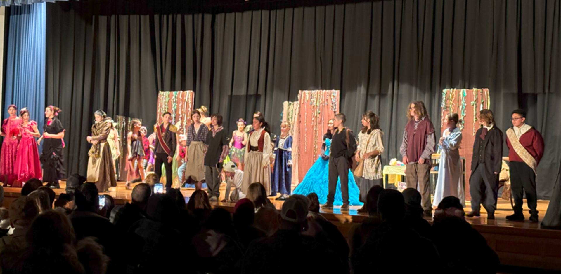 Students perform on stage in costumes at a theater event.