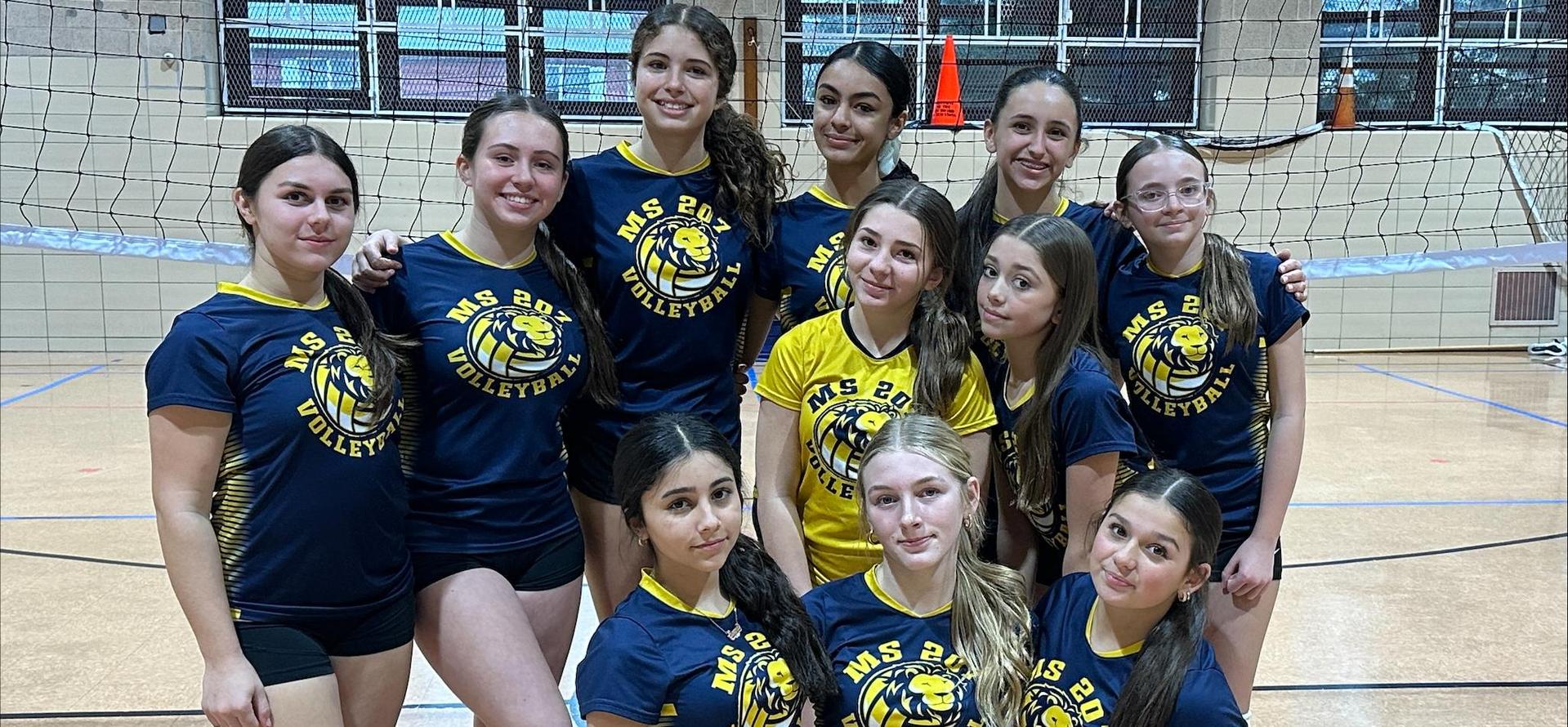 A group of young female volleyball players posing together in a gym.