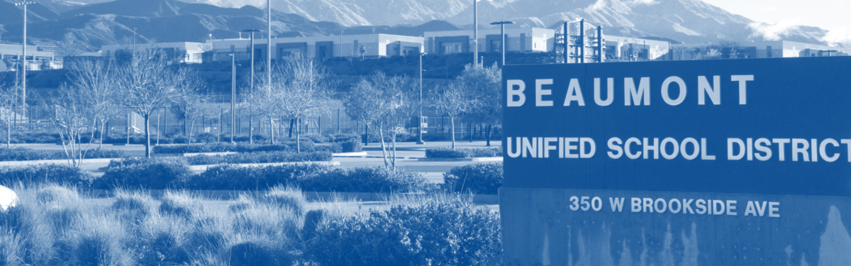 A block wall with the words "Beaumont Unified School District" with trees and the District Office parking lot in the background.