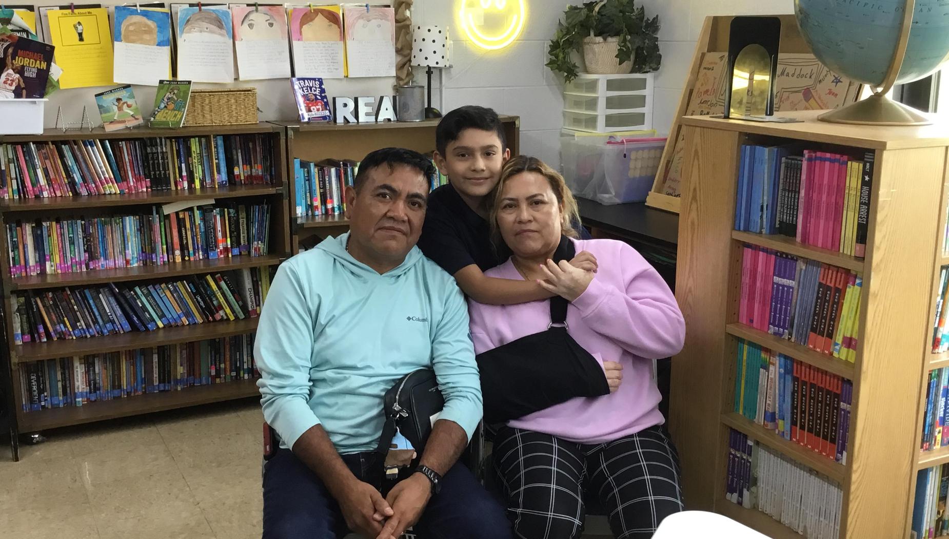A boy is embraced by his parents in a bright library, surrounded by books and cheerful decor.
