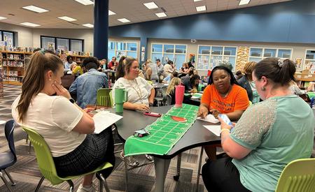 A large group of people working together at tables in a vibrant library setting.