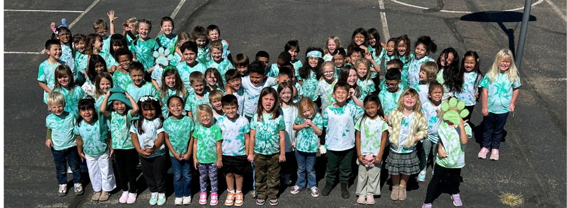 BES students in green tie-dye shirts smiling together outdoors.