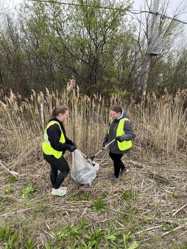 Two volunteers collecting litter in the grass near tall reeds.