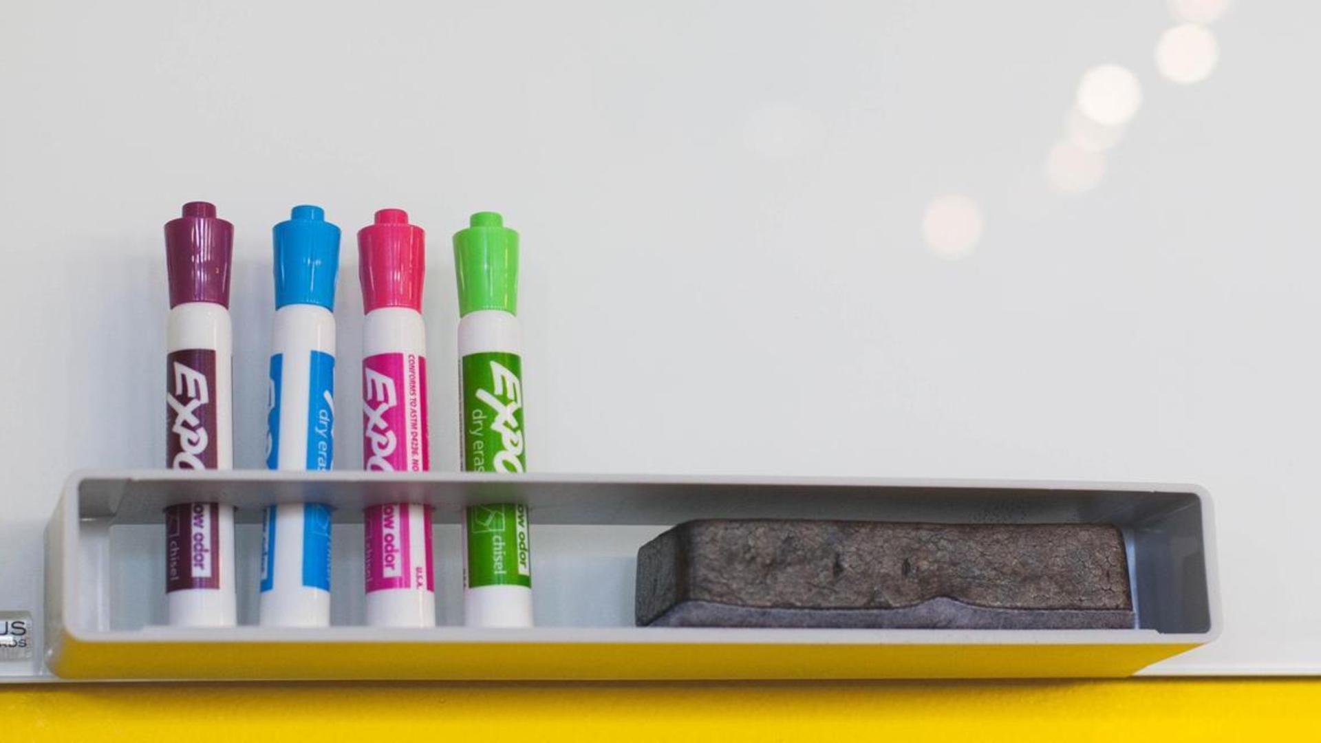 Four markers and an eraser on a whiteboard tray.